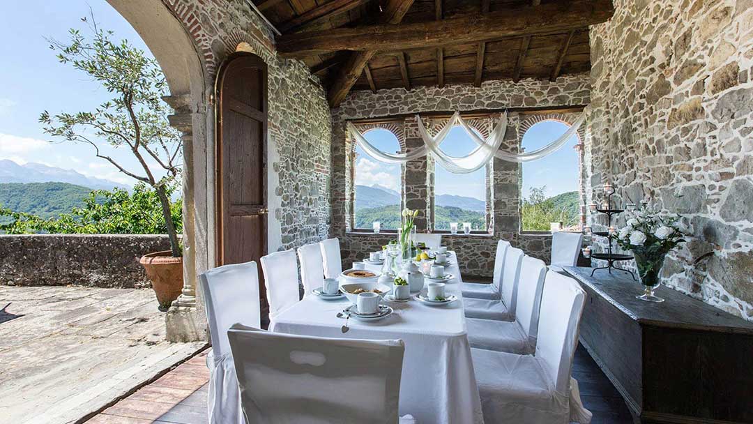 Sala da pranzo di Villa Raffaelli in Garfagnana, Toscana, con tavolo elegante, muri in pietra, vista panoramica. Fascino storico e comfort moderni per vacanze indimenticabili.